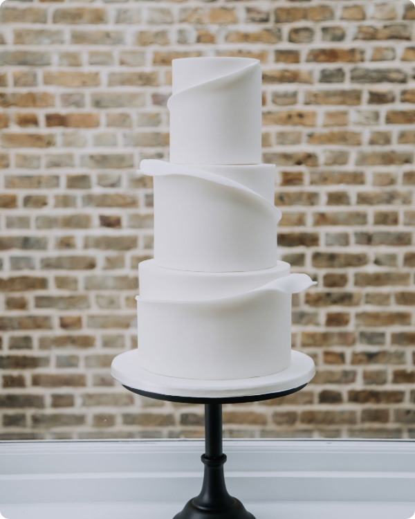 Modern white three tier cake with wrap around frill and black pedestal cake stand.